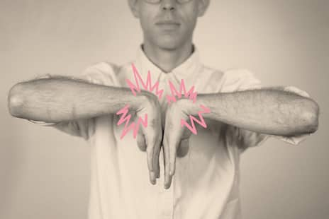 A photo illustration that shows a man holding his arms out to the side with the outside of his wrists pressed against each other in front of his chest. There are illustrated pink, jagged lines around his wrists.